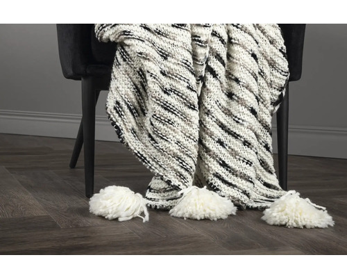 Grovstickad pläd med tofsar på en stol