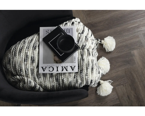 Dekorativ scen med en tidning, en skål och en stickad filt med tofsar på en fåtölj.