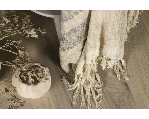 Dekorativ tyg med fransar draperat över ett sidobord, bredvid en blomvas.