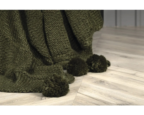 Närbild av en olivgrön stickad filt med tofsar.