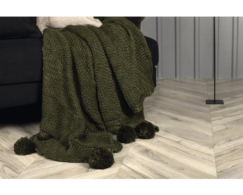 Grön stickad filt med tofsar på en soffa