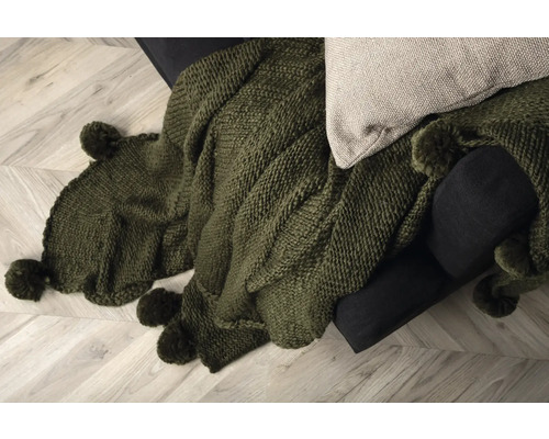 Närbild av en grön stickad filt med tofsar på en soffa