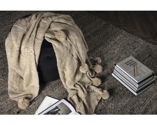 Dekorativ stickad filt med tofsar på pall och matta