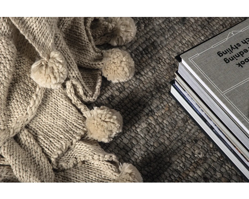 Dekorativ scen med stickad filt med tofsar, matta och bokstapel