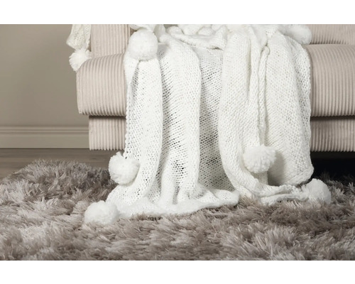 Mjuk pläd med tofsar på en soffa och matta