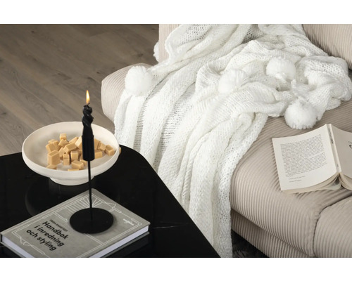 Dekorativt vardagsrum med stickad filt, ljus och bok på bordet