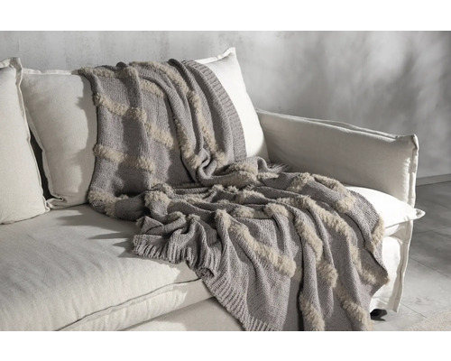 Grå överkast med dekorativa element på en soffa.