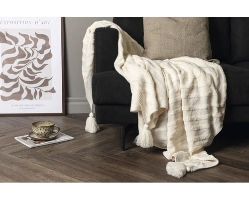 Scen med ett ljust överkast på en soffa, en konsttryck och en kopp på en tidning.