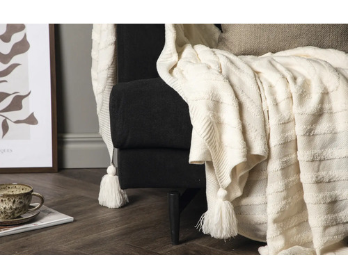 Närbild av en fåtölj med en stickad filt med tofsar