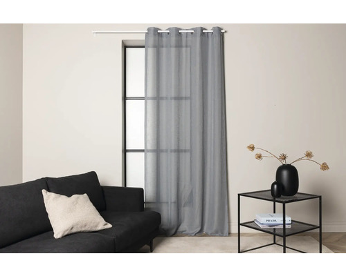 Vardagsrum med soffa, sidobord och grå gardin framför ett fönster.