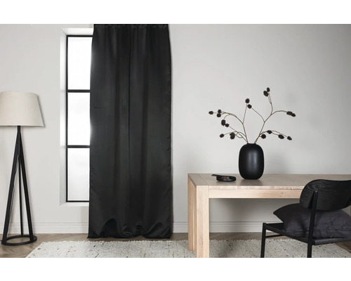 Ljust rum med svart gardin, golvlampa, bord och stol.