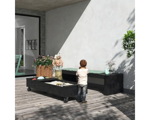 Uteplats med sandlåda på hjul, träbänkar med dynor och lekande barn.