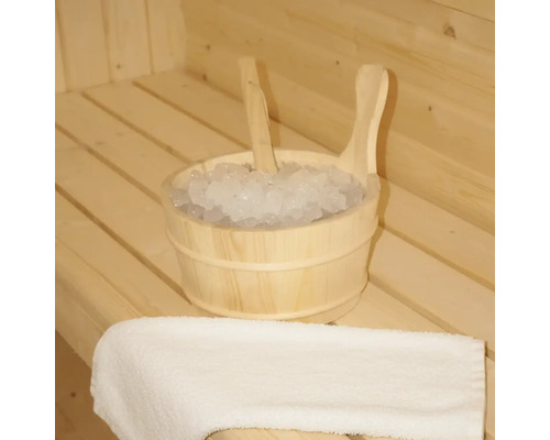 Trä hink med is och en skopa i en bastu, bredvid en handduk.