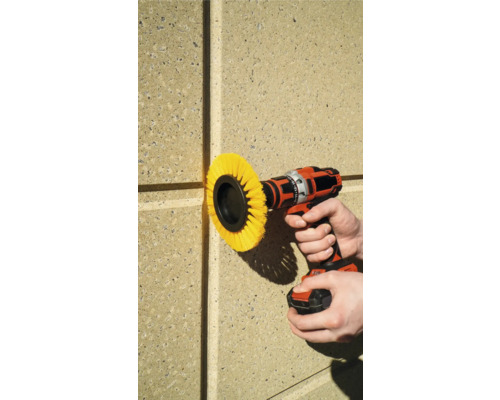 En borrmaskin med borstfäste används på en husvägg.