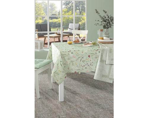 Dukat matbord med blommig duk, stolar och mat i ett ljust rum.