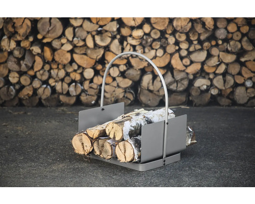 Vedkorg av metall med vedträn framför en stapel ved