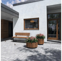 Uteplats med träbänkar och runda planteringskärl framför ett modernt hus.