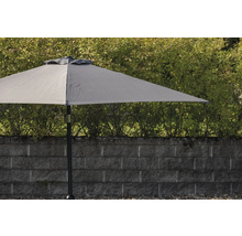 Grått trädgårds parasoll med mast framför en stenmur