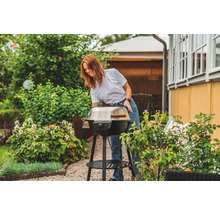 Kvinna förbereder en klotgrill i trädgården.