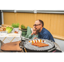 Scen med en pappa och ett barn som grillar korv i trädgården.