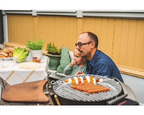 Scen med en pappa och ett barn som grillar korv i trädgården.