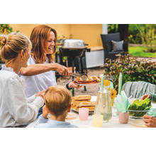 Familjens grillfest i trädgården med korv, potatis och tillbehör på bordet.