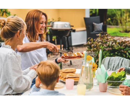 Familjens grillfest i trädgården med korv, potatis och tillbehör på bordet.
