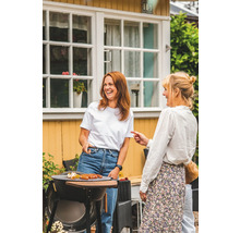 Två kvinnor står vid en grill i trädgården och grillar korv.