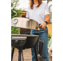 Kvinna öppnar locket till en elektrisk grill i trädgården.