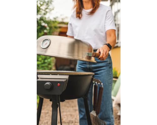 Kvinna öppnar locket till en elektrisk grill i trädgården.