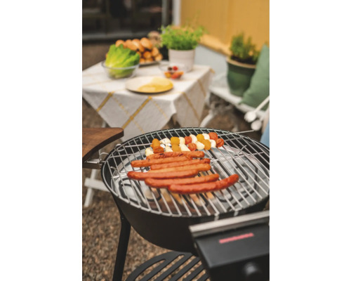 Grill med korvar och grönsaksspett, trädgårdsbord i bakgrunden