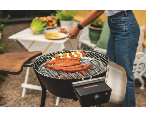 Elektrisk grill med korvar och grönsaksspett på grillgallret, i trädgården.