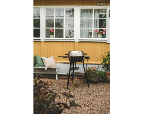 Klotgrill i trädgården framför ett hus med vita fönster och gul fasad.