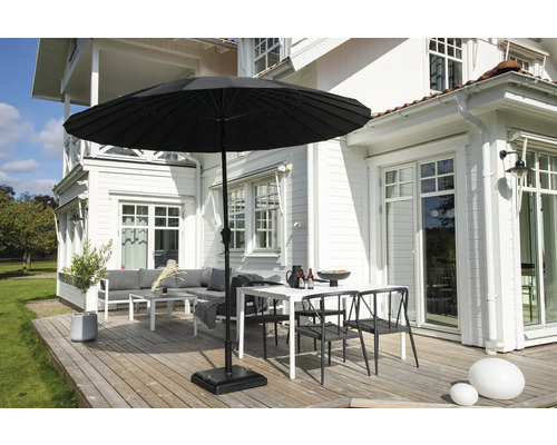 Trädgårdsscen med parasoll, bord, stolar och loungeset på en träaltan framför ett vitt hus