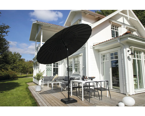 Svart parasoll på en terrass med trädgårdsmöbler framför ett hus