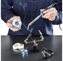 Person löder kablar med lödkolv, lödtenn och flussmedel på en arbetsyta.