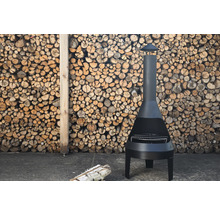 Svart trädgårdskamin med grillgaller framför en stapel ved