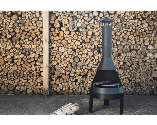 Svart trädgårdskamin med grillgaller framför en stapel ved