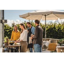 Människor grillar utomhus under ett parasoll på terrassen.