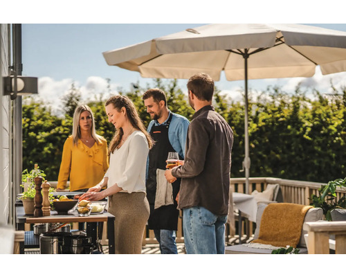 Människor grillar utomhus under ett parasoll på terrassen.