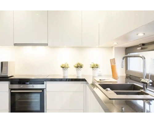 Ljust kök med vita skåp, svart bänkskiva, diskho och kokplatta.