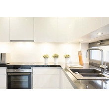 Modernt kök med vita skåp, mörk bänkskiva, diskho och elektriska apparater.