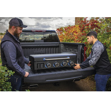 Två personer lastar en svart gasolgrill i en lastbil.