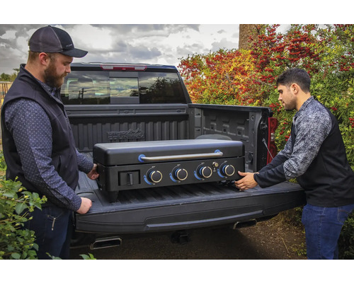 Två personer lastar en svart gasolgrill i en lastbil.