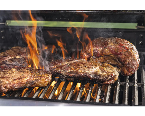 Flera biffar på en grill med öppen låga.