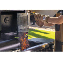 En person tömmer en skorstenständare med glödande grillbriketter i en grill.