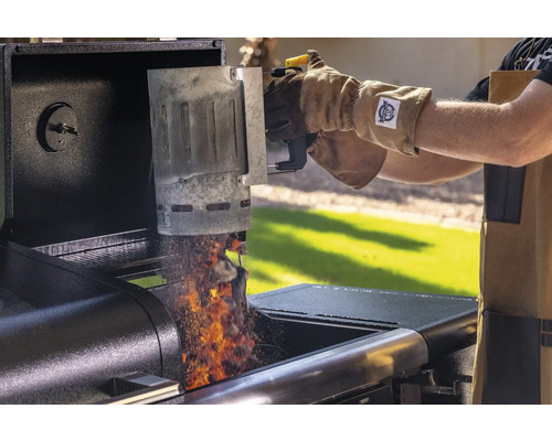 En person tömmer en skorstenständare med glödande grillbriketter i en grill.