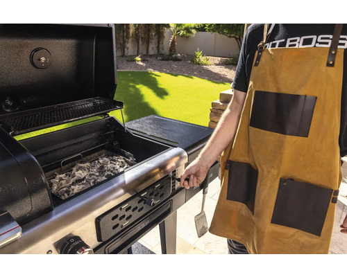 Grill med öppet lock, kol och person med grillförkläde