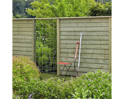 Trädgårdsutsikt med trästaket, spaljé, trädgårdsredskap och trädgårdspall