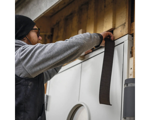 En man fäster en tätningsremsa på en dörr för att täta den.